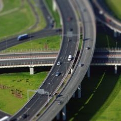 Vairāku līmeņu ceļu pārvadi un automašīnas Rīgā no augšas ar miniatūras efektu.