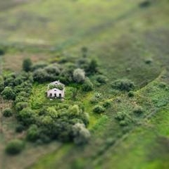 Nelielas ēkas drupas koku un pļavu ieskautā vietā aerofotogrāfijā ar miniatūras efektu.